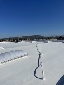 A flat white rooftop with several domed skylights and a metal pipe running across the surface, set against a clear blue sky and distant hills.