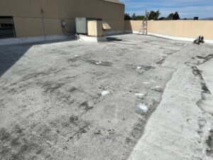 Flat rooftop with a weathered surface, HVAC unit, ladder, and some scattered equipment. Shadows and patch marks are visible on the roof.